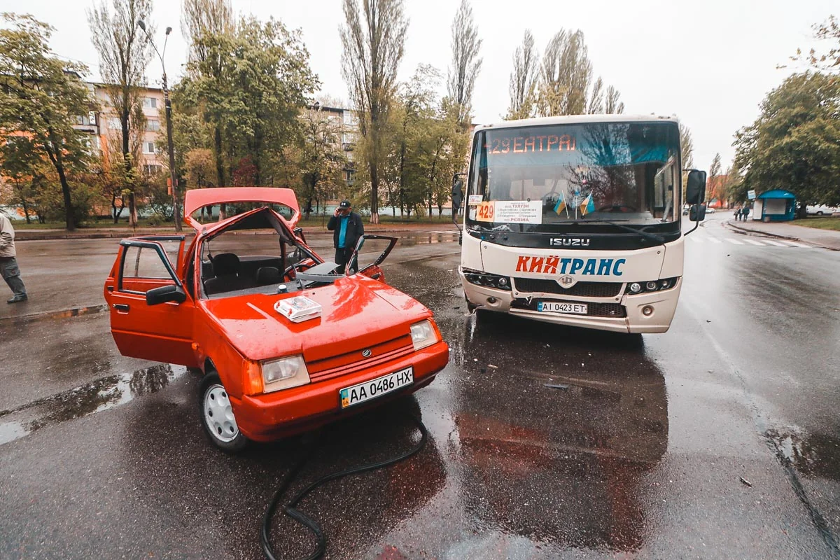 Пошкоджений червоний легковик і автобус Кийтранс після ДТП на мокрій дорозі
