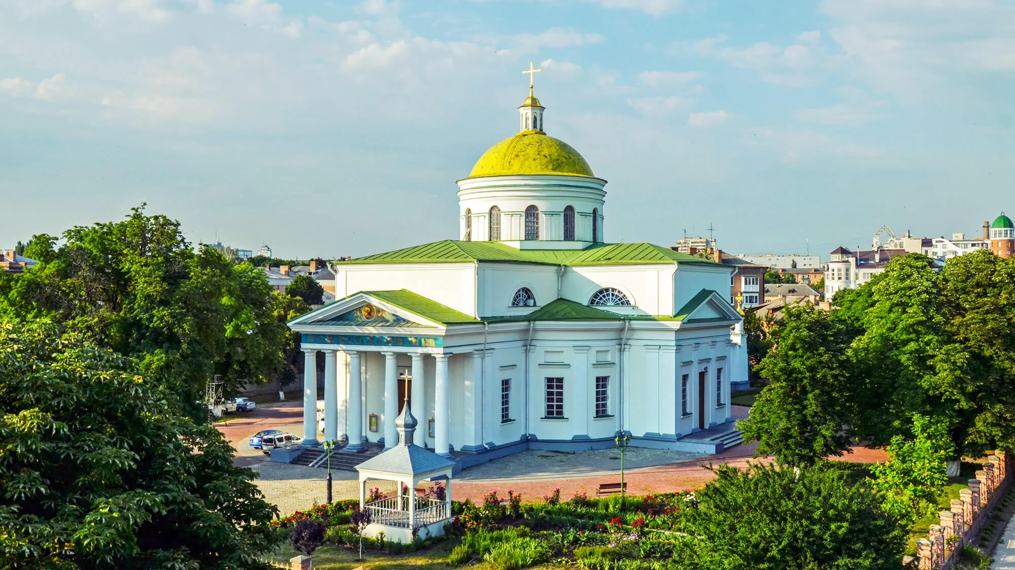 Білий класицистичний собор із золотим куполом і колонадою серед парку