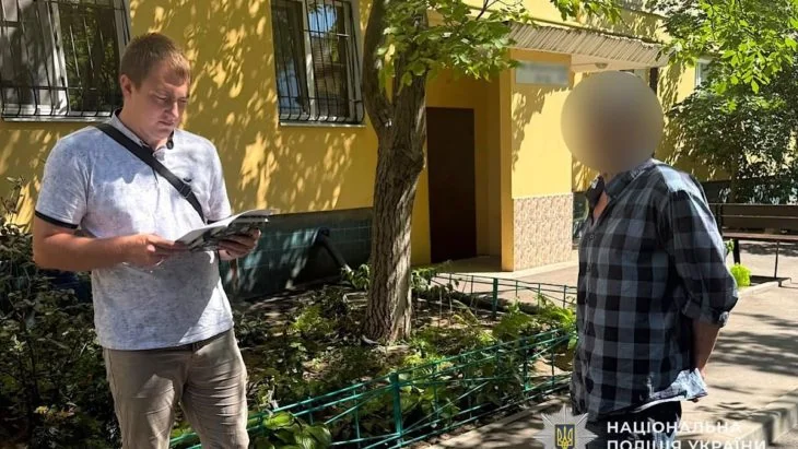 Поліцейський читає блокнот поруч із чоловіком із розмитим обличчям біля жовтої будівлі