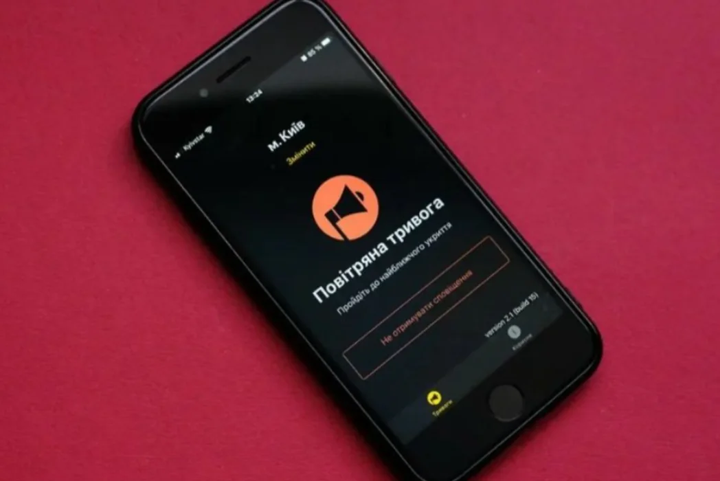Чорний смартфон на бордовому тлі показує додаток повітряної тривоги Києва