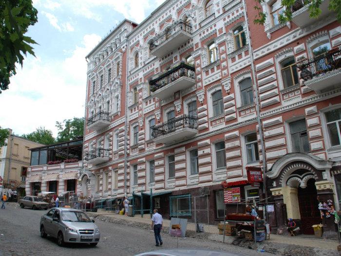 Історична червоно-біла будівля з балконами на брукованій вулиці Києва