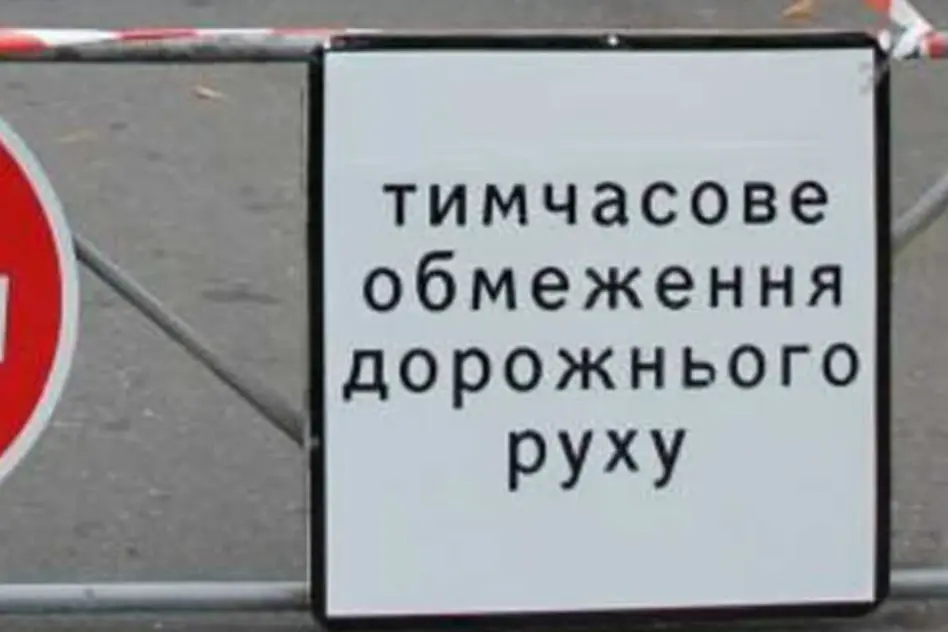 Білий знак «тимчасове обмеження дорожнього руху» біля бар’єра і червоного круга