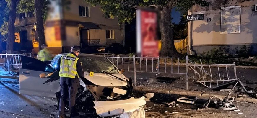 Поліцейський оглядає розбитий білий автомобіль після нічної ДТП