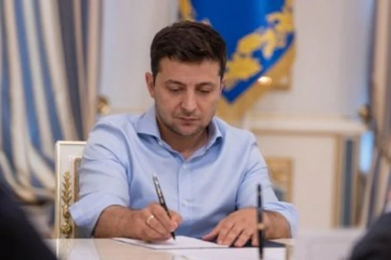 Володимир Зеленський підписує документ за столом у президентському кабінеті