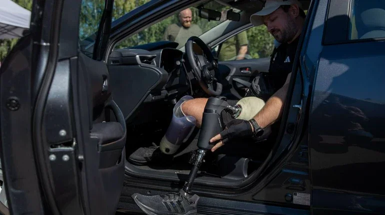 Чоловік із протезами ніг сідає в легковий автомобіль біля відкритої двері