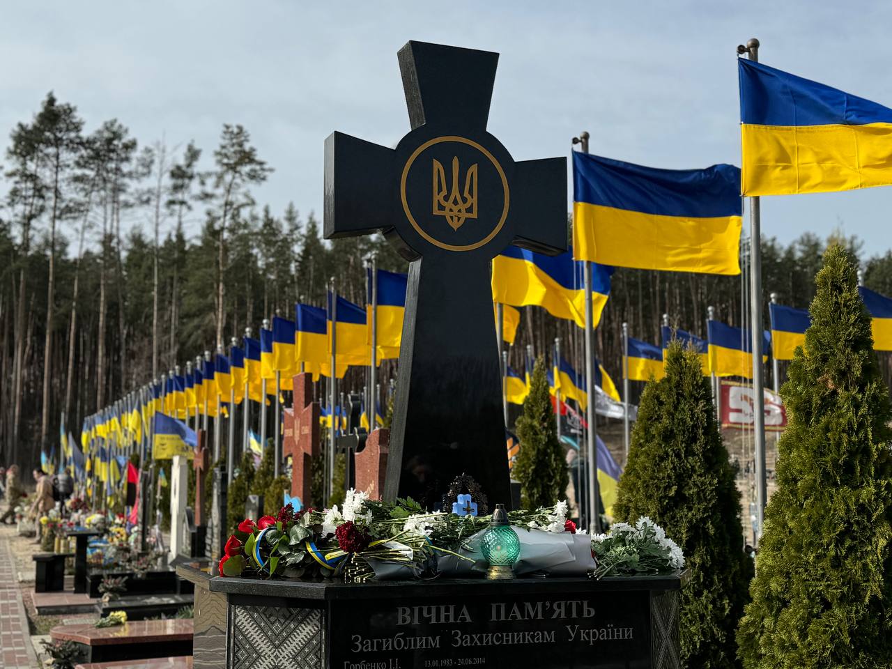 Меморіальний цвинтар захисників з чорним хрестом, тризубом і рядами українських прапорів