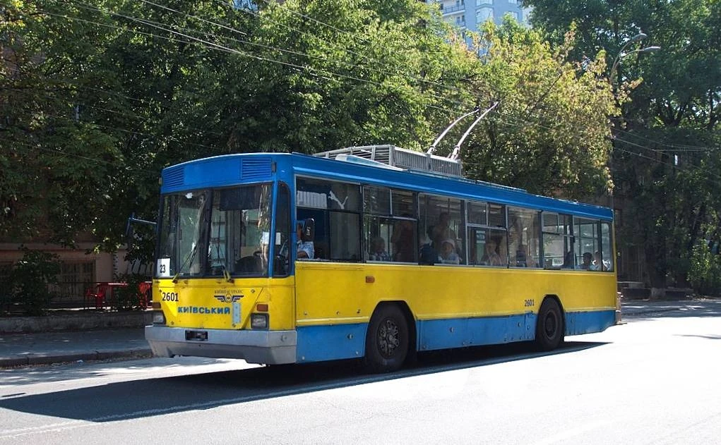 Жовто-синій тролейбус на зупинці серед зелені