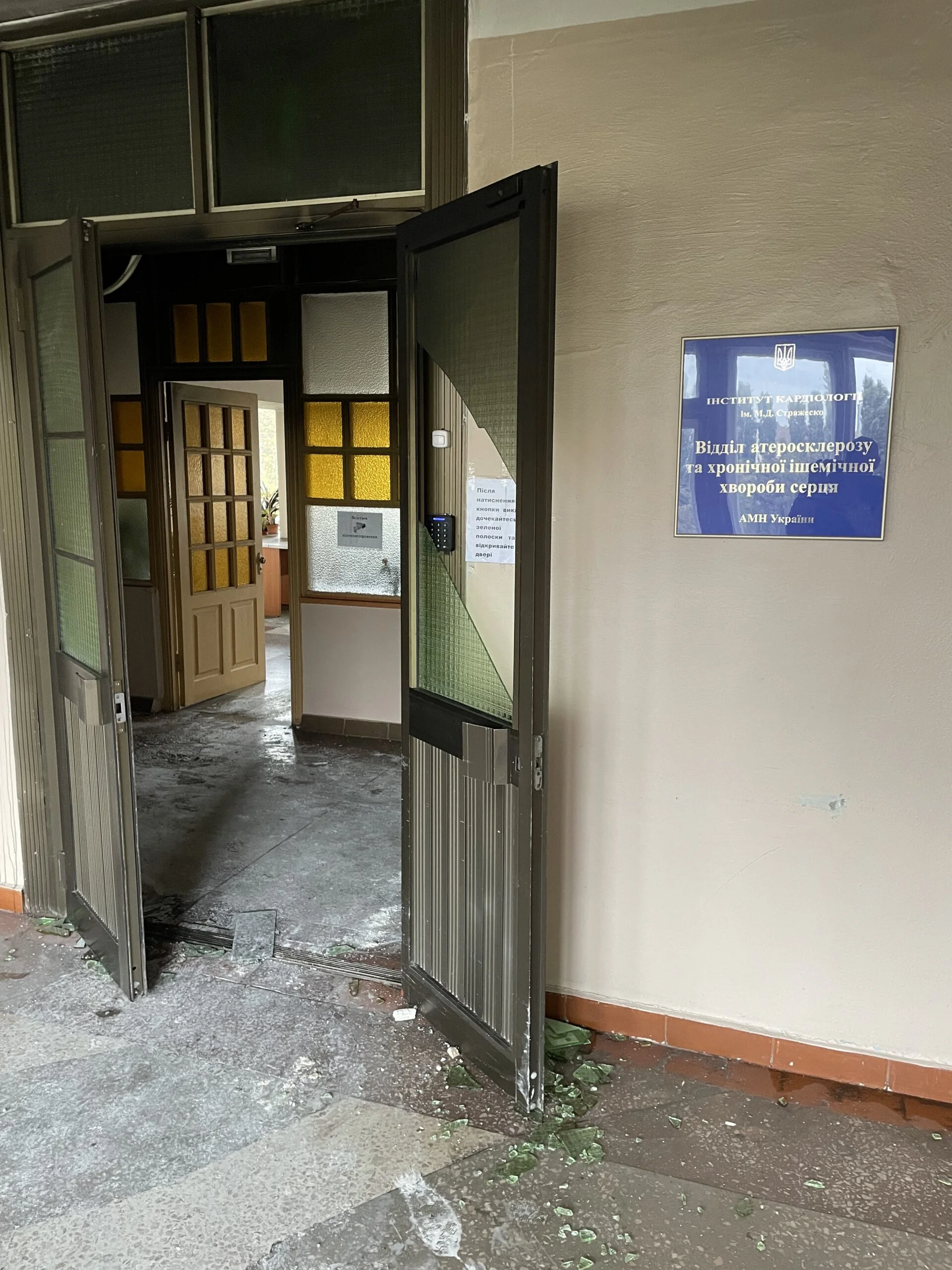 Відчинений вхід Інституту кардіології Стражеска з осколками скла та синьою вивіскою відділу